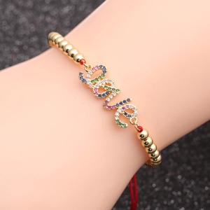 Gold beaded bracelet with red woven cord and colorful zircon LOVE charms on a wrist
