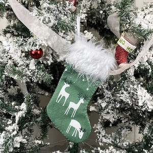 Green Christmas stocking with white reindeer prints and faux fur trim on a snowy tree