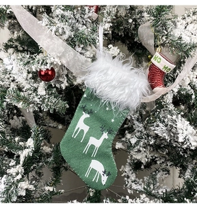 Detail of a green reindeer Christmas stocking hanging on a snow-covered tree branch