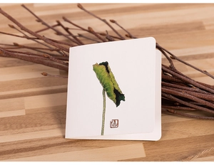 Detail of a minimalist white card with lotus leaf illustration and red seal on wood desk