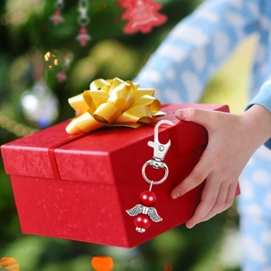 Silver metal angel wings keychain with red beads shown on a Christmas gift box