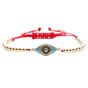 Macro detail of red woven chain bracelet with blue zircon evil eye charm in gold