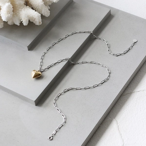 Close-up of dual-tone paperclip chain with 3D gold heart pendant on white background