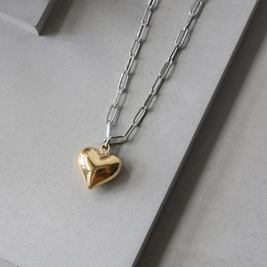 Close-up of golden heart pendant on silver paperclip chain with polished metallic texture