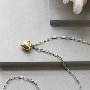 Close-up of gold 3D heart pendant on silver paperclip chain against stone background