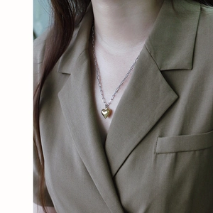 Detail of a two-tone heart pendant with silver paperclip chain worn on a model