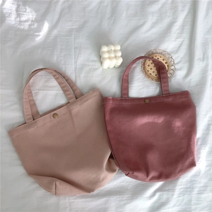 Detail of pink canvas tote bags with metal button closure on soft white fabric background