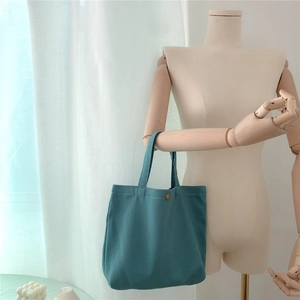 Detailed view of teal twill canvas tote bag featuring a vintage round metal button closure