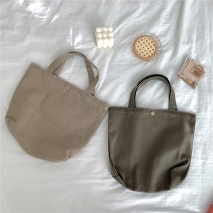Detail of minimalist canvas tote bags in khaki and olive with metal snap button closure