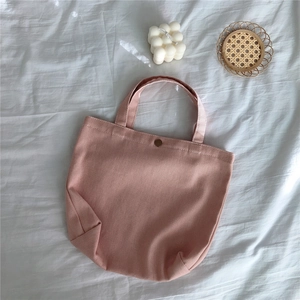 Detailed view of a pink canvas handbag with metal snap closure on a textured white fabric