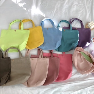 Detailed flat lay of colorful canvas tote bags with metal snap buttons on a white bed sheet