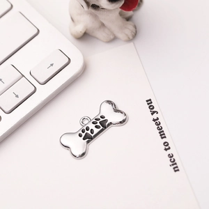 Zinc alloy bone dog tag featuring a black paw print charm on a desktop setting