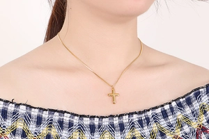 Detail of minimalist gold cross necklace with sleek snake chain on female model