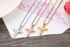 Detailed view of 3D cross necklaces in silver, rose gold, and gold on a white envelope