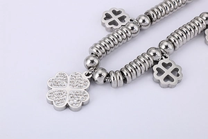 Macro shot of silver metal charm bracelet featuring clover pendants with zircon inlay