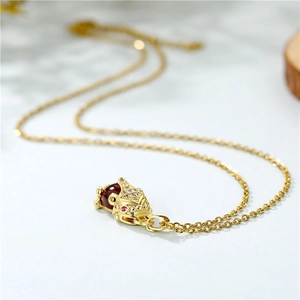 Golden PiXiu necklace with red bead and crystal zircon pendant on textured surface