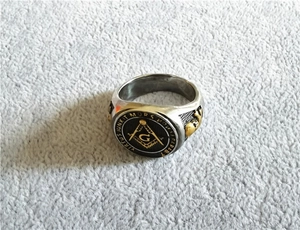 Gros plan sur bague maçonnique en acier avec compas doré et gravure latine