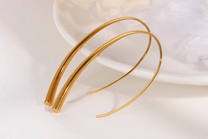 Macro shot of long U-shaped minimalist gold earrings on white ceramic plate