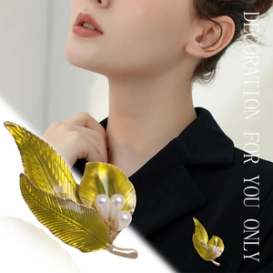 Elegant gold leaf brooch with green enamel and white pearl shown on garment and detail