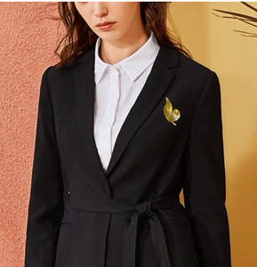 Detailed view of a golden leaf brooch with white accents on a black blazer lapel