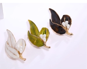Detail of enamel leaf brooches with gold finish and pearls in white, green, and brown