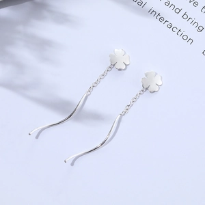 Macro detail of silver four-leaf clover drop earrings with wavy wire and delicate chain