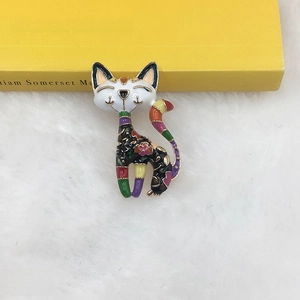 Close-up of colorful enamel cat brooch with floral patterns on a white plush surface