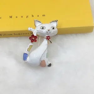 Detailed close-up of a white enamel Egyptian cat brooch with floral accents on a book