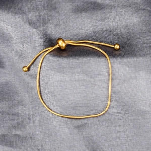 Detail of adjustable gold snake chain bracelet with sliding ball clasp on textured background