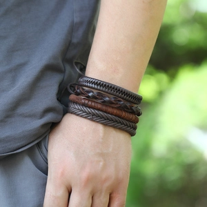 Detail of layered brown leather woven bracelets shown on model against a natural background