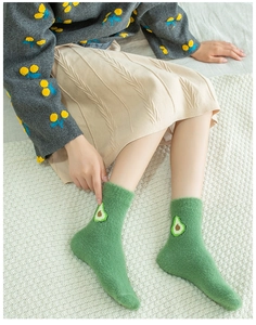 Close-up of green fuzzy winter socks with avocado embroidery and warm plush texture