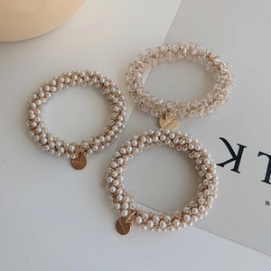 Detailed view of woven pearl hair ties with gold brand charms on minimalist background