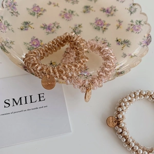 Close-up of pearl and crystal beaded hair ties with small metal tags on a floral plate
