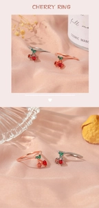 Detailed view of cherry rings with red gemstones and green leaves on pink satin fabric