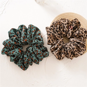 Detail of two leopard print scrunchies in orange and brown on a woven coaster