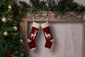 Close-up of two red knitted Christmas stockings with white reindeer patterns on a mantel