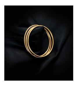 Macro shot of polished gold triple-intertwined bangles on black leather background