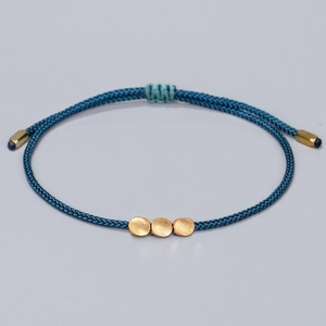 Handmade woven navy blue Tibetan bracelet with three gold beads on a grey background