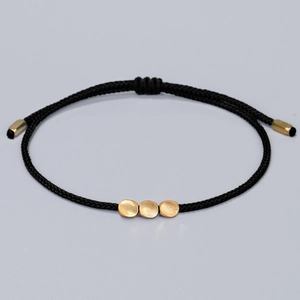 Handwoven black string bracelet featuring three matte gold beads with adjustable closure