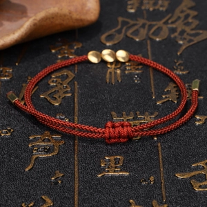 Detail of red handmade braided bracelet with golden beads on a vintage cultural base