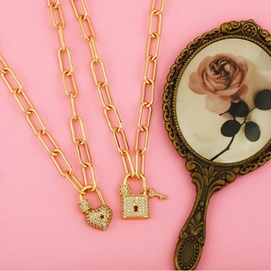 Collier chaîne dorée avec pendentifs cœur et cadenas sertis de zircons sur fond rose doux