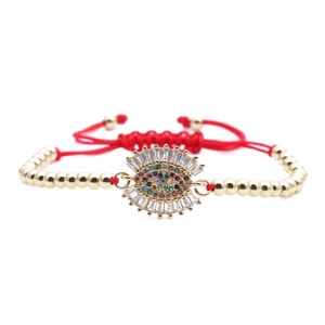 Macro detail of red woven chain bracelet featuring a gold zircon evil eye charm