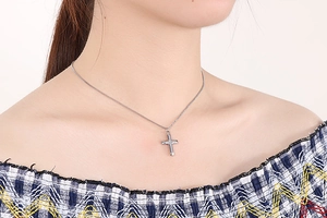Close-up of a polished silver cross pendant necklace worn by a model on a curb chain