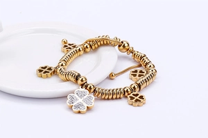 Detail shot of a gold clover charm bracelet with white crystals on a white ceramic plate