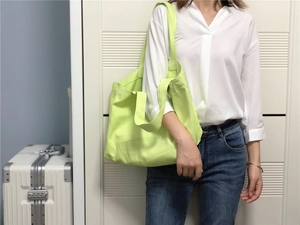 Detail van de neongroene canvas draagtas getoond met een wit shirt en een koffer