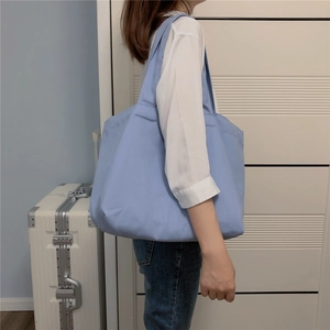 Detail van een grote lichtblauwe canvas tas met brede schouderbanden aan een model