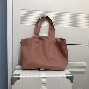 Detail van oudroze canvas shopper met drukknoop geplaatst op een witte rolkoffer