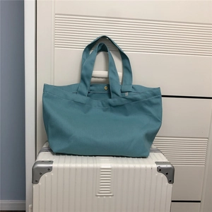 Detail van groenblauwe canvas shopper met gouden drukknoop op een witte koffer