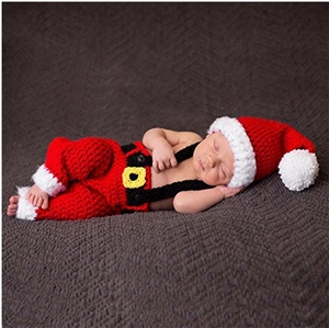 Detailed knit of newborn Christmas photo outfit with red hat and suspender pants on rug