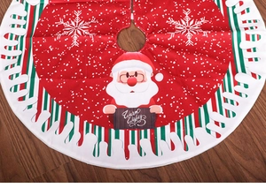 Detail of red Christmas tree skirt with Santa Claus motif and Warm Wishes text on wood floor